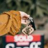 A hand holds keys in front of a blurred sold real estate sign, symbolizing completed sale.